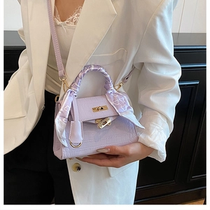 Close-up of light purple crocodile pattern handbag with floral scarf and gold twist lock