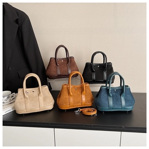 Detail view of five trapezoidal suede handbags in beige, brown, black, yellow, and navy