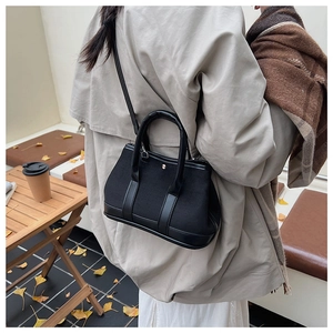 Model wearing a black canvas bucket bag with leather trim in a cozy autumn cafe setting