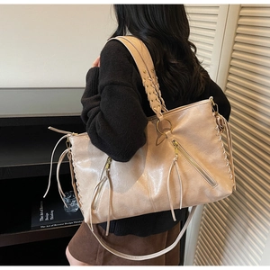 Detail view of the beige leather tote bag featuring woven straps and decorative tassels