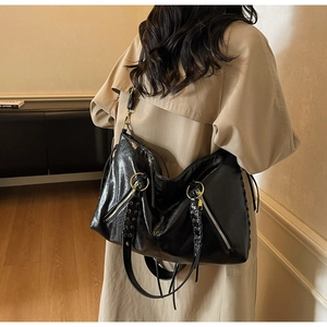 Detail of glossy wrinkled leather tote with gold rings and woven strap on a trench coat