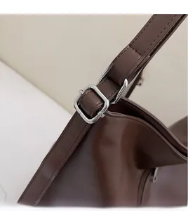 Detail of dark brown leather tote showing silver metal buckle and adjustable long strap