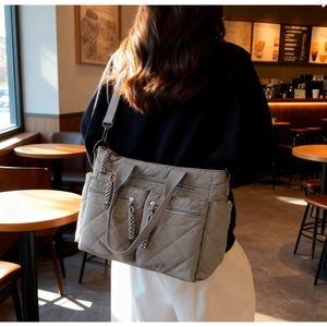 Detail of grey quilted tote bag with dual front zippers and wide shoulder strap