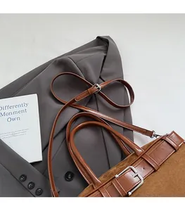 Close-up of brown suede shoulder bag with adjustable strap and metal buckle detail