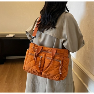Detailed side view of a large orange quilted nylon crossbody bag with woven zipper pulls