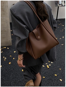 Deep brown lychee textured leather tote bag carried by a model in an urban setting