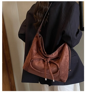 Détail du sac hobo en daim marron foncé avec nœud décoratif sur un costume à rayures