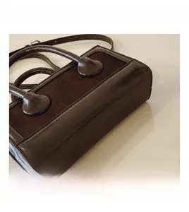 Detailed close-up showing coffee brown suede and glossy leather textures on the handbag