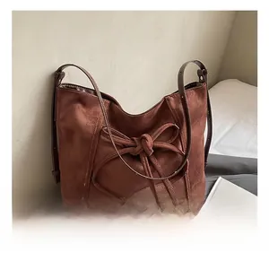 Détail du sac à bandoulière en daim marron avec nœud décoratif et sangle en cuir
