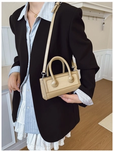 Detail of a beige minimalist small square bag with rounded handles and silver hardware