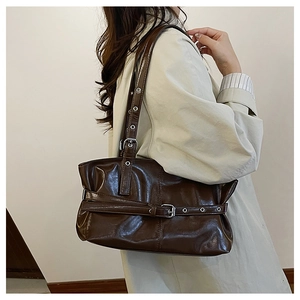 Detail of dark brown glossy leather tote bag with metal eyelets and strap buckles