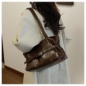 Detail of dark brown glossy leather shoulder bag featuring decorative buckle and metal eyelets