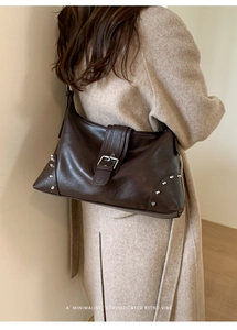 Close-up of retro brown leather tote with silver rivets and buckle on a beige coat
