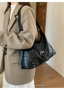 Detail of vintage black leather bag with silver studs and buckles on beige coat