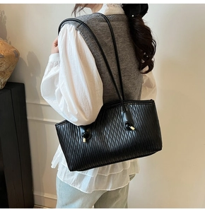 Détail du cabas noir avec plis ondulés verticaux et accents métalliques dorés