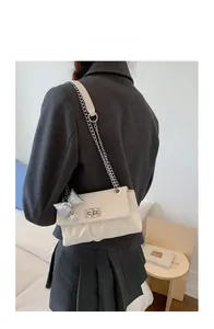 Detail view of cream pleated square bag with silver chain strap and metal bow charm