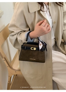 Detalle del bolso Kelly en ante marrón oscuro con cierre dorado y asa con pañuelo de seda