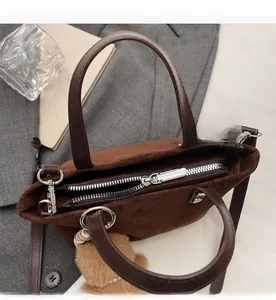 Detail view of smooth silver zipper closure and plush bear charm on dark brown suede tote