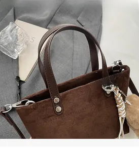 Close-up of suede handbag with leather handle, silver rivets, and plush charm detail
