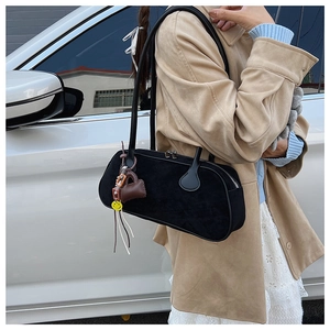 Close-up of black suede baguette bag with double thin straps and cute charms on a shoulder
