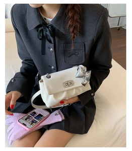 Detail view of white pleated crossbody bag featuring a silver butterfly heart charm
