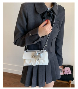 Detail of white pleated crossbody bag with silver bow charm and metal chain strap