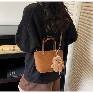 Dettaglio di una borsa a secchiello scamosciata marrone con ciondolo a forma di orsetto