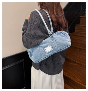 Detail of light blue denim tote bag with metal plaque showing over-the-shoulder carry style