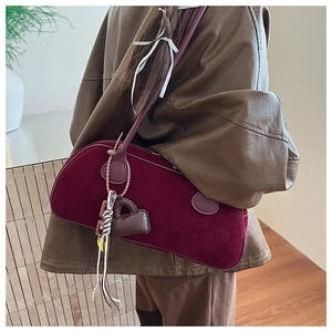Detail of burgundy velvet baguette bag featuring brown leather strap and heart charm decor