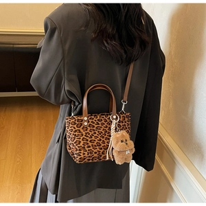 Detail of leopard print bucket bag with dark brown leather handle and cute plush dog charm