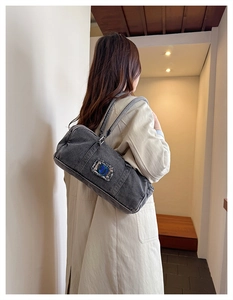 Detail of dark grey washed denim shoulder bag featuring a holographic logo plate decoration