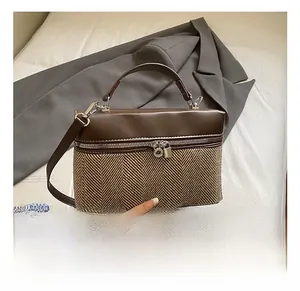 Detail of color-block herringbone handbag featuring brown leather trim and metal clasp