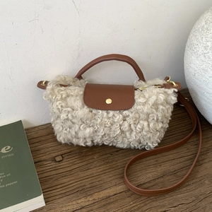 Detailed texture of white faux shearling bag with brown leather strap and gold button