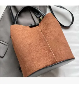 Close-up of brown suede and black leather bucket bag with gold hardware on a grey blazer