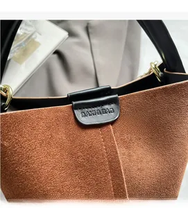 Detail of brown suede bucket bag with embossed logo flap and metallic ring hardware
