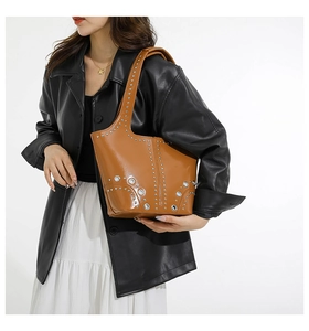Detail of studded brown leather shoulder bag with metallic eyelets on white background