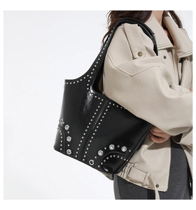 Detail of black glossy leather shoulder bag with silver studs and metal eyelets on model