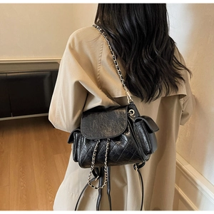 Détail d'un mini sac à dos en cuir matelassé noir avec chaînes dorées sur un modèle