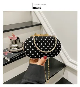 Close-up of black and white polka dot bag with gold bow clasp and metal chain strap