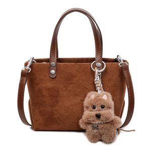 Brown suede tote bag with leather straps and a plush dog charm on a white background