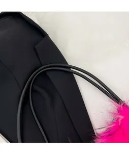 Detail of black shoulder bag featuring adjustable strap and pink faux fur charm