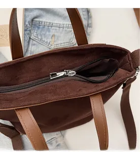 Detail shot of the smooth black zipper closure on a brown suede tote bag