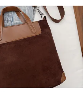 Detail of dark brown suede tote bag featuring leather stitching and adjustable strap