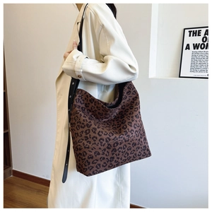 Large leopard print tote bag with wide strap worn by model in a modern interior setting