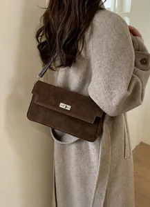 Detail of dark brown suede shoulder bag with silver metal buckle on beige wool coat