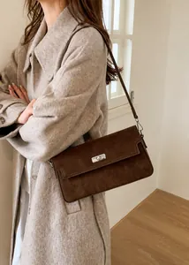 Detail of a dark brown suede shoulder bag with a silver swivel clasp on a wool coat