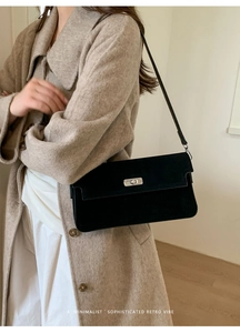 Detail of a black suede-textured rectangular shoulder bag with silver twist lock
