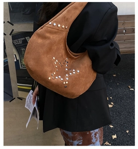 Detail of brown suede hobo bag with silver star studs carried by model in urban setting