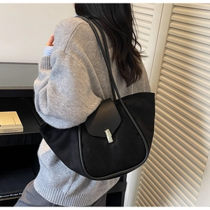 Detail of black winged bucket bag with silver buckle worn over a model shoulder