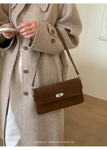 Detail of a dark brown suede crossbody bag with silver metal buckle on a beige wool coat